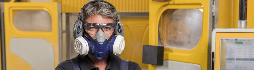 Fabricator wearing protective gear including a respirator mask, safety glasses, and earmuffs, standing confidently in a Caesarstone workshop.
