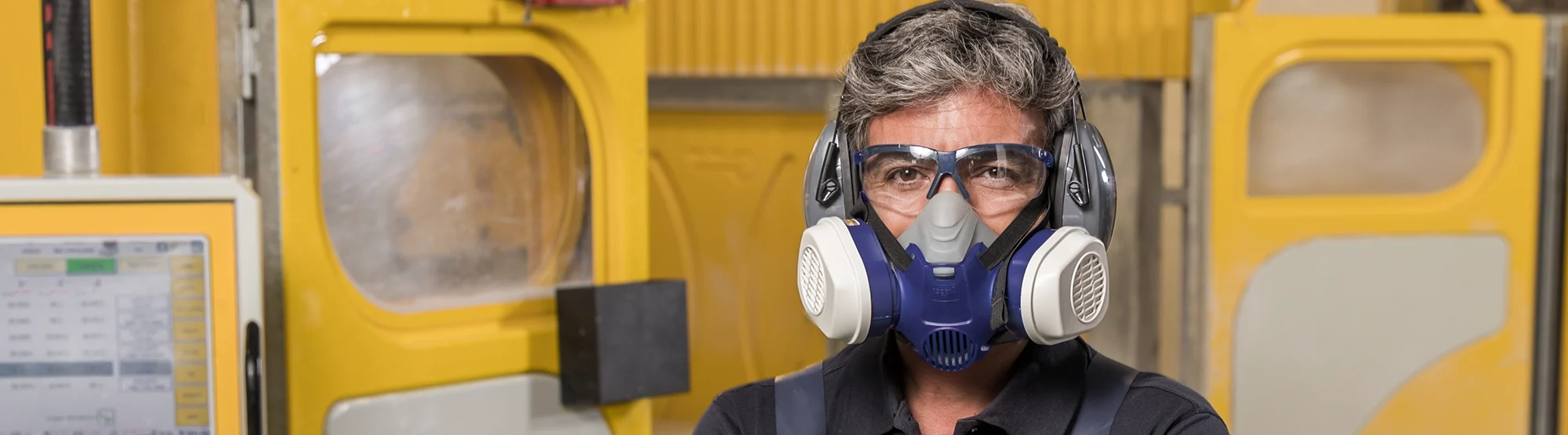 Fabricator wearing protective gear including a respirator mask, safety glasses, and earmuffs, standing confidently in a Caesarstone workshop.