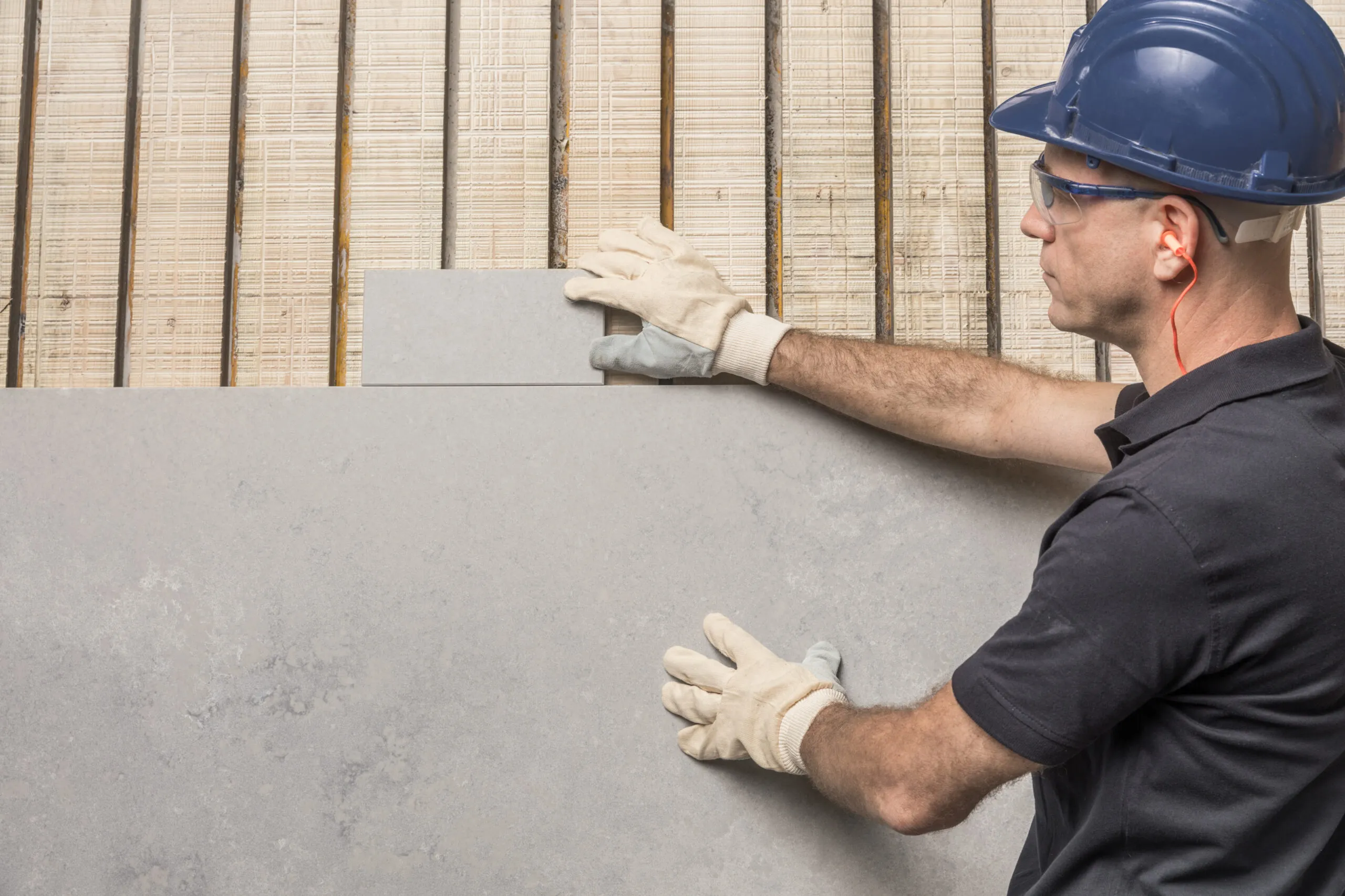 Worker wearing safety gear installing a large gray stone slab.