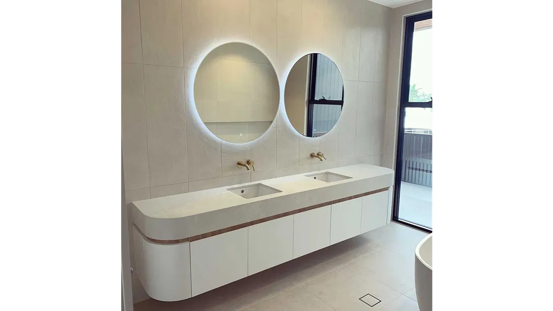 Modern bathroom with a curved Caesarstone thermoformed vanity top, dual sinks, and round backlit mirrors.