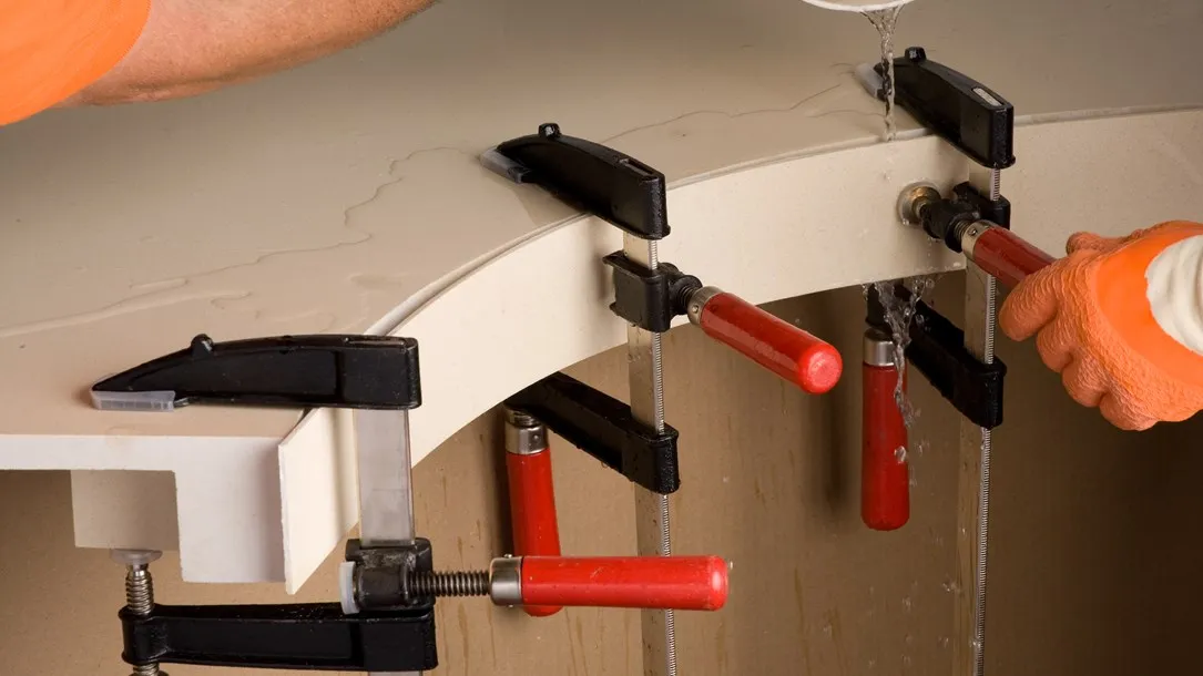 Fabricator shaping a curved Caesarstone quartz surface with clamps and water during the thermoforming process.