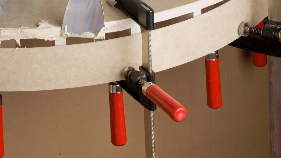 Fabricator applying adhesive to a curved Caesarstone quartz surface held by clamps during the thermoforming process.