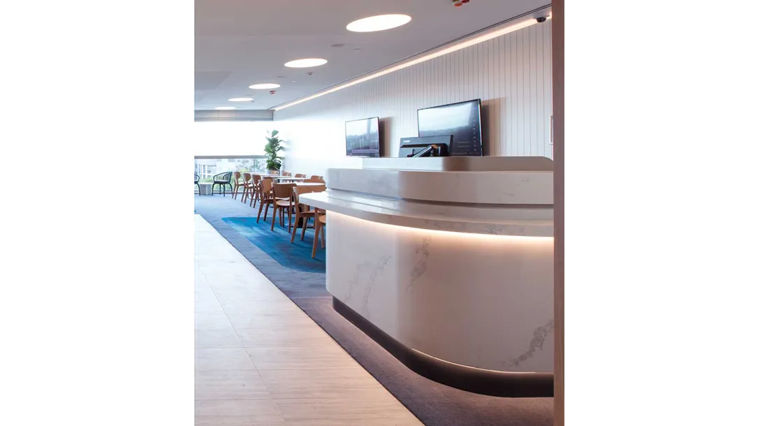 Curved white Caesarstone quartz reception counter with soft lighting in a modern office or dining space, demonstrating thermoformed surface design.