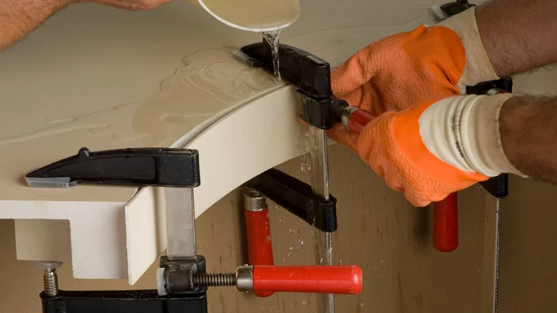 Worker using clamps and resin to join curved quartz countertop pieces.