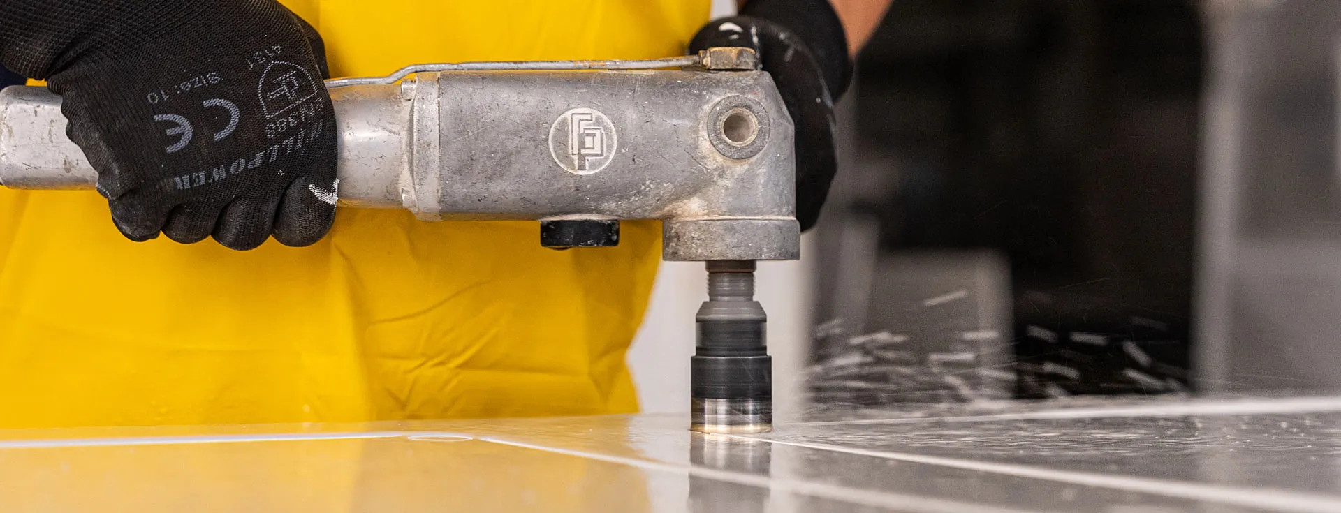 Worker polishing a Caesarstone slab with a power tool, wearing a yellow protective apron and black gloves.