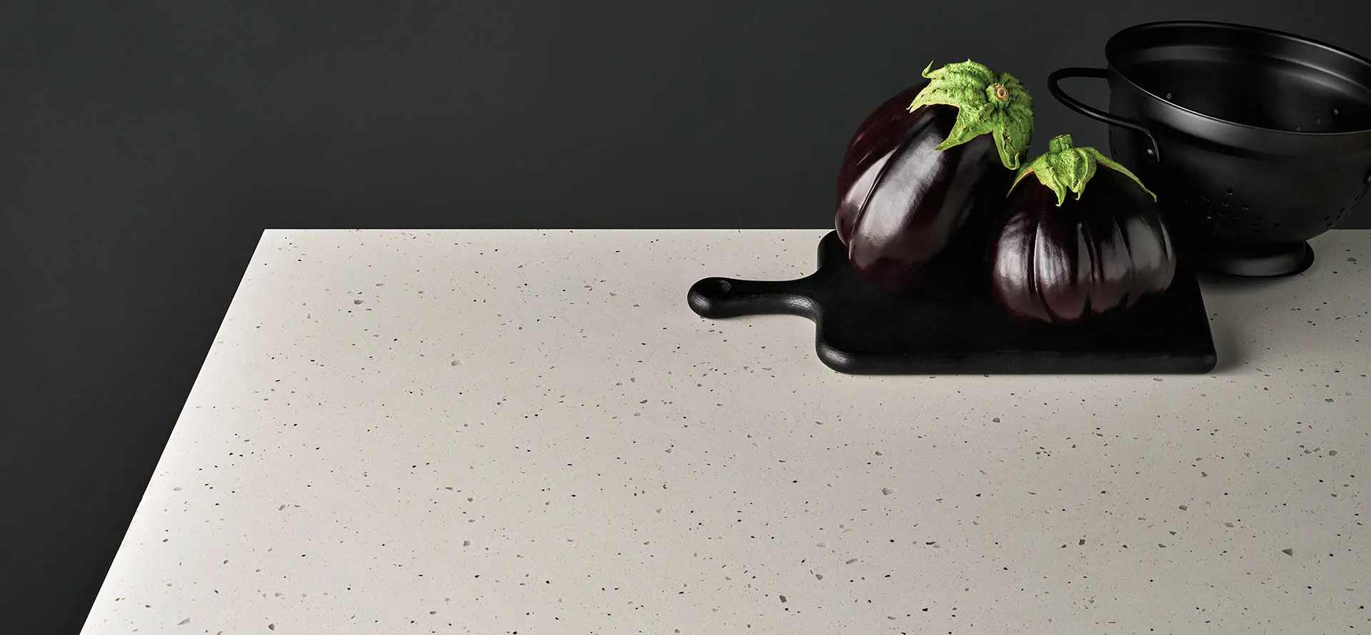 Comptoir en quartz Caesarstone au motif moucheté clair, mettant en scène des aubergines sur un fond noir.